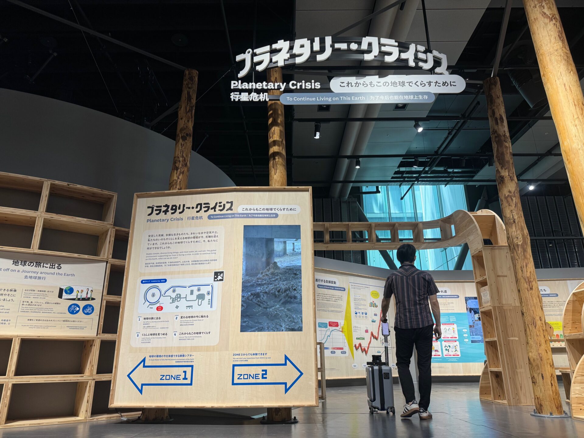 にっぽん科学未来館の常設展示、プラネタリー・クライシスのいりぐちでエーアイスーツケースを片手に立つしらとりさんのうしろすがたの写真