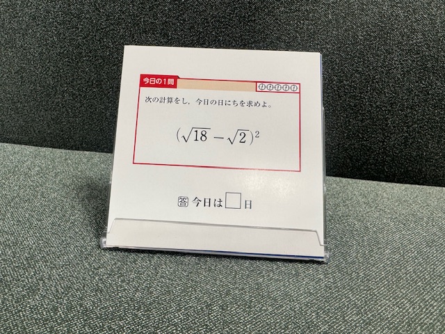 ケースにいれられた、ひめくりの一枚をうつした写真。このひの問題わ、かっこルート18、マイナス、ルート2かっことじのじじょうが問題としてかかれています