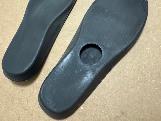 左右のくろいインソールのうらがわの写真。左足だけ、かかとのほうにまるいくぼみがあります