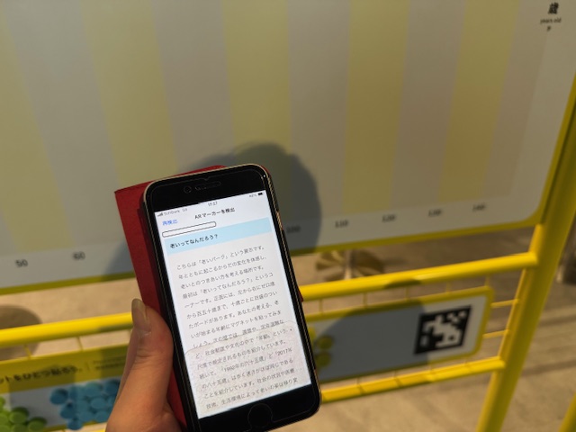 常設展示、老いパークのARマーカーをにっぽんかがくみらいかんアシストアプリで読み取った様子を写した写真。ARマーカーはQRコードのような形状で、これをアプリでスキャンして読み取ります。スマホの画面にはARマーカーから検出された「おいってなんだろう?」についての説明テキストが表示されています