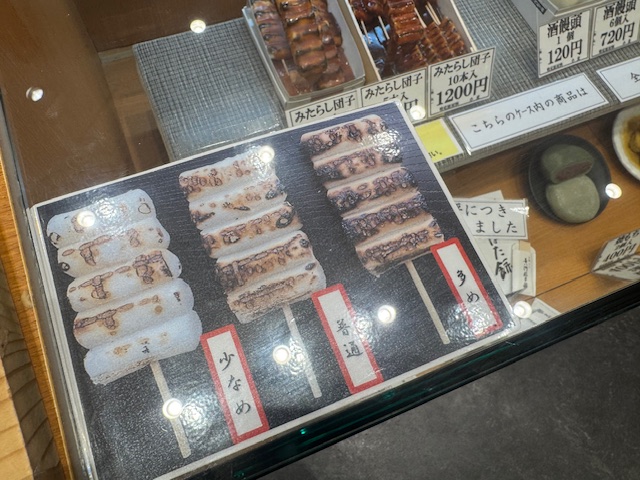 ショーケースにハラれた、やきかげんを三段階から選べるみたらしだんごの写真。みたらしをつけるまえの写真です。すくなめわすこしこげめがつく程度、おおめになるにつれてこげめの面積がふえていきます。おおめわぜんたいてきにこげめのほうが多いくらいです