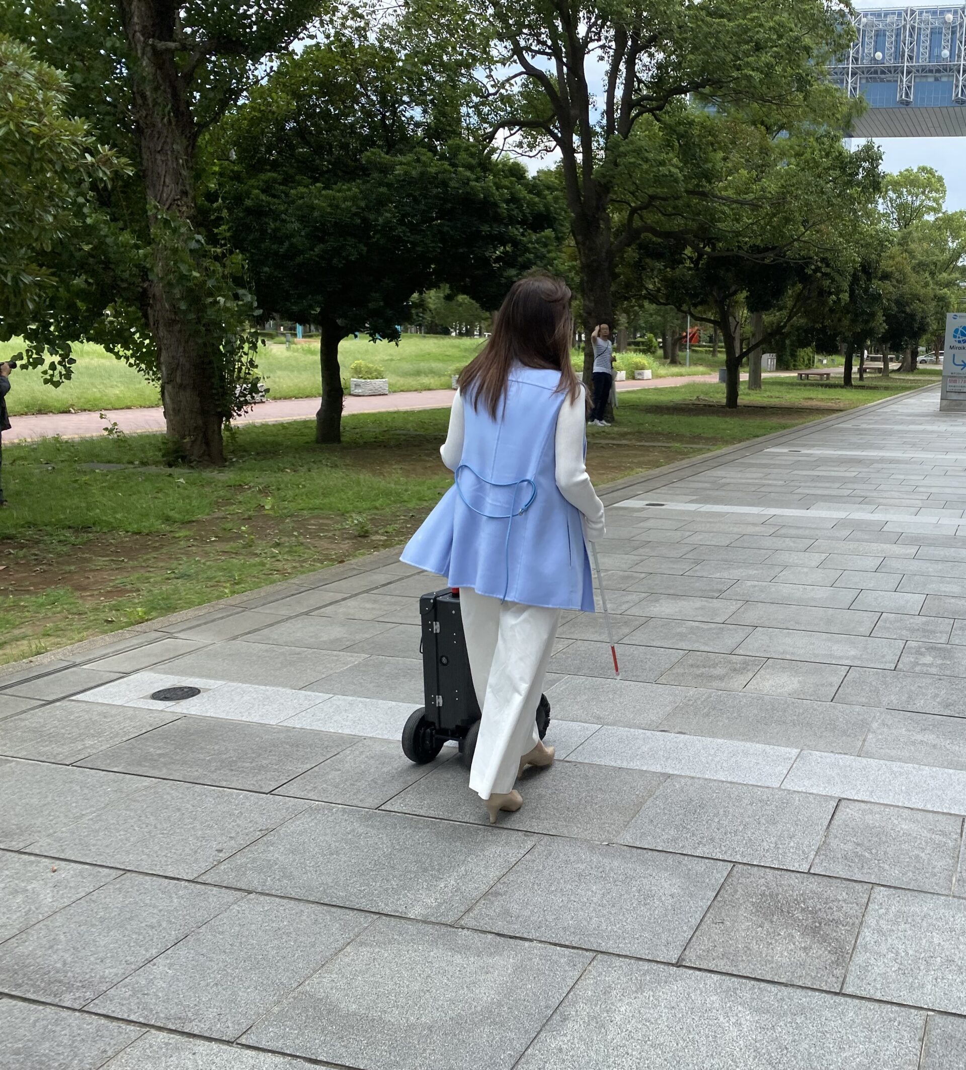 右手にはくじょう、左手にエーアイスーツケースのハンドルをもって歩くあさかわしの後ろ姿の写真