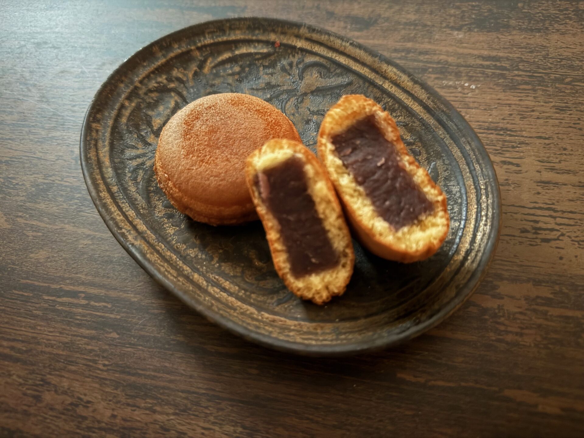 茶色とゴールドのおさらにのった、ふたつのまるいにんぎょうやきの写真。ひとつわはんぶんにわれていて、ちゅうおうにこしあんがぎっしりつまっています