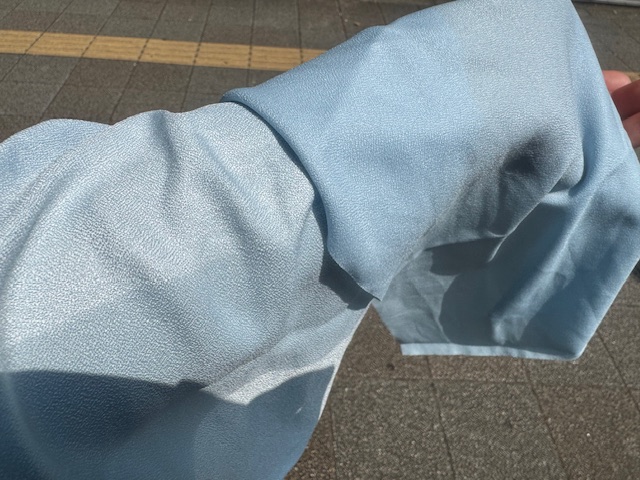屋外で半分だけぬらしたライトブルーのひんやりタオルをうでにのせた写真。ぬれているほうがぬれていないほうにくらべて、すこしだけブルーが濃くなっていますが、言われないとわからない程度です