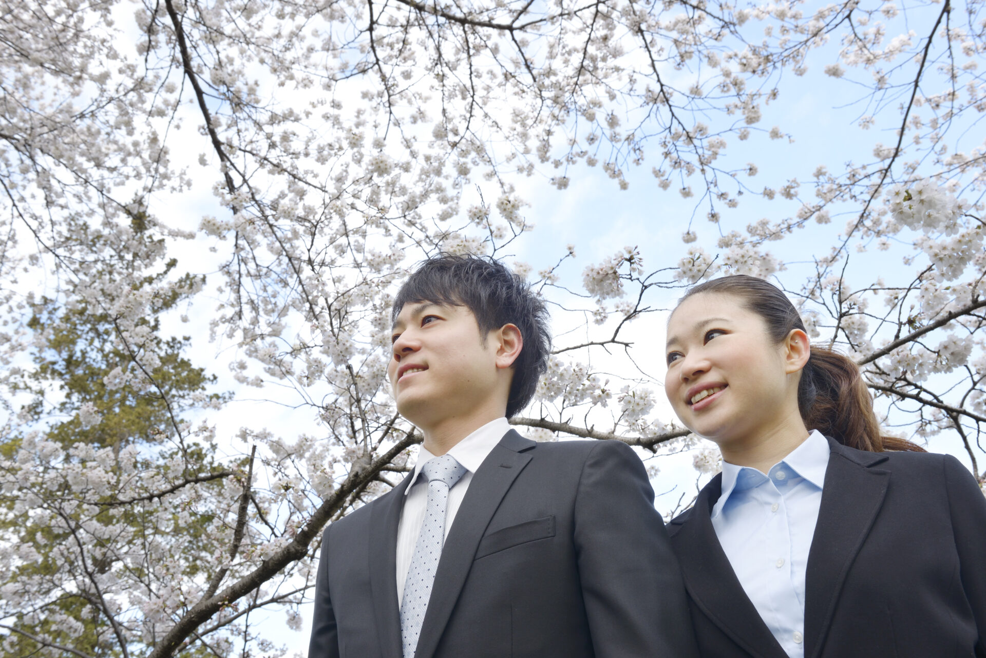 桜の花をバックに笑顔で佇む希望に満ちた新入社員の写真