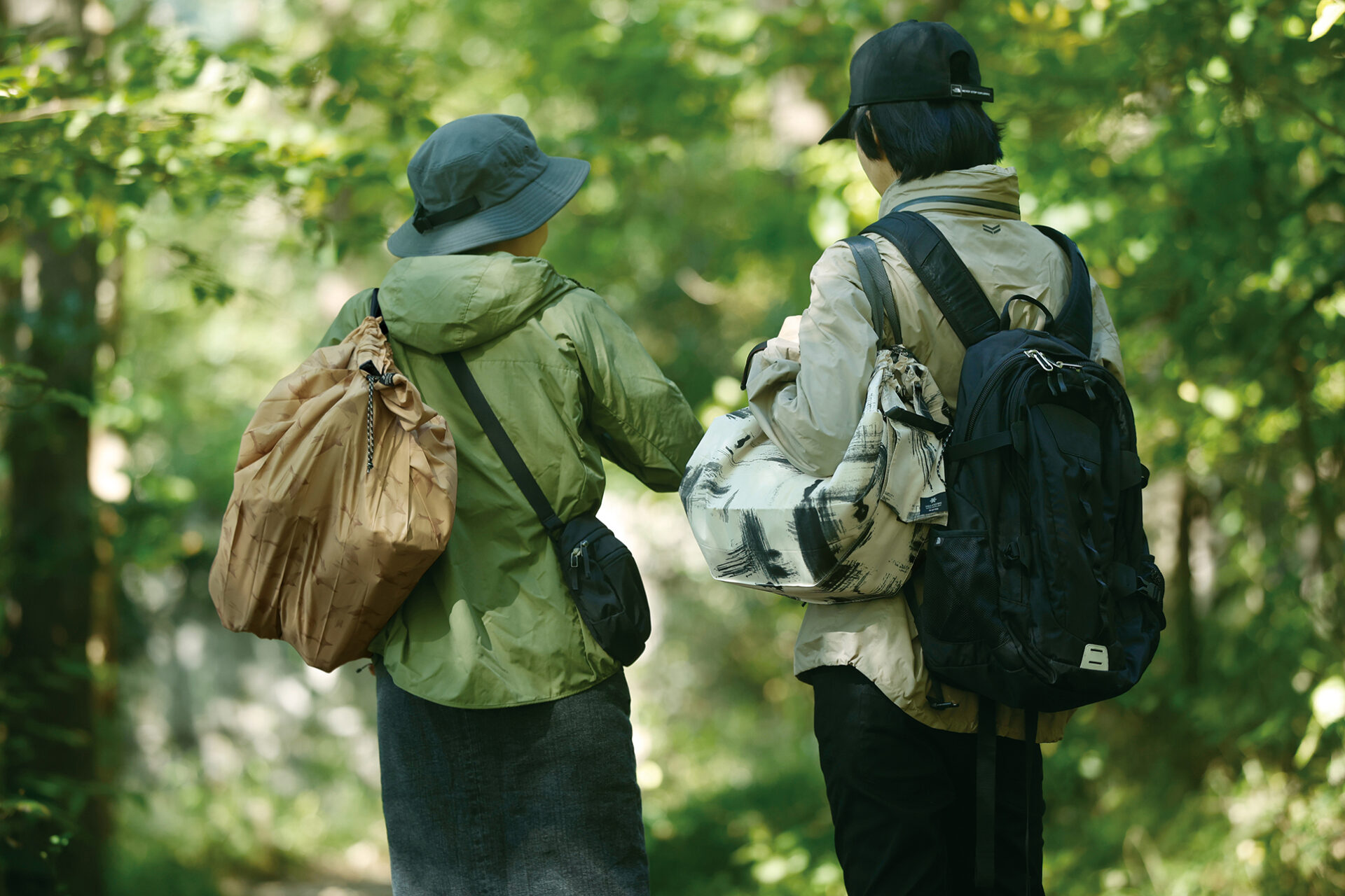 シュパットの新しいシリーズ「ライトアウトドア」のバッグを持って森の中を歩いているふたりのうしろ姿の写真