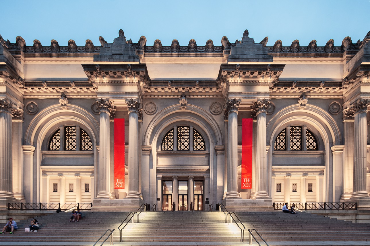 アメリカ、ニューヨークのメトロポリタン美術館の外観写真。歴史を感じる立派な建物の前に大階段があり、座っている人もいます